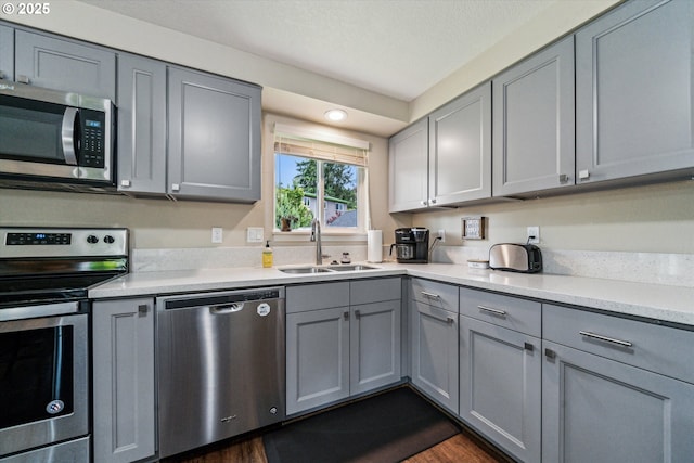 kitchen with appliances with stainless steel finishes, gray cabinetry, a sink, light countertops, and dark wood finished floors