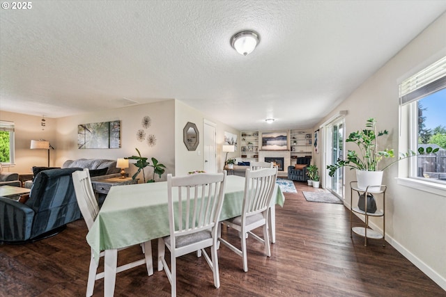 dining area with a warm lit fireplace, dark wood-style floors, healthy amount of natural light, a textured ceiling, and baseboards