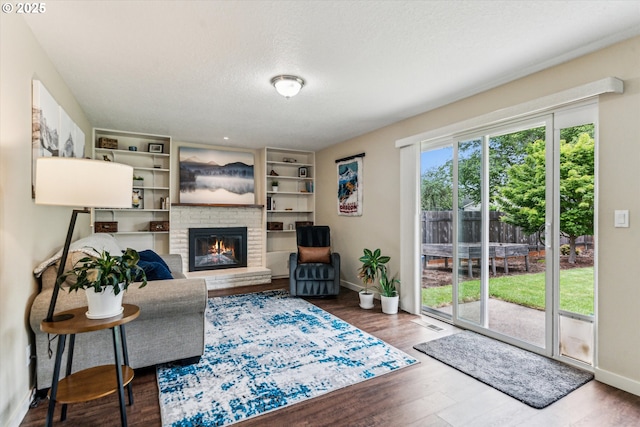 living room featuring a fireplace, a textured ceiling, baseboards, and wood finished floors