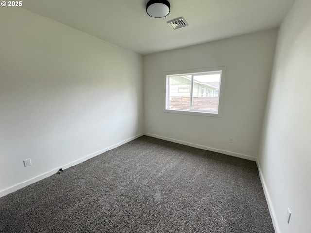 spare room with baseboards, dark colored carpet, and visible vents