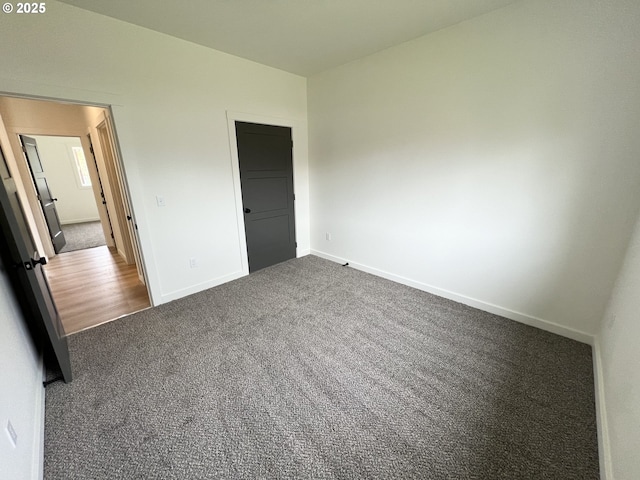 unfurnished bedroom with dark carpet and baseboards