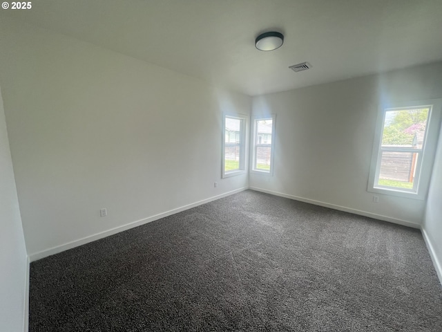 empty room featuring visible vents, baseboards, a healthy amount of sunlight, and dark colored carpet