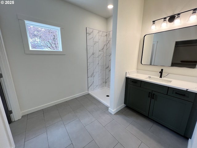 bathroom with vanity, baseboards, a tile shower, and tile patterned flooring