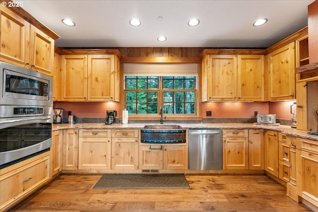 kitchen featuring appliances with stainless steel finishes, a sink, recessed lighting, wood finished floors, and light brown cabinets