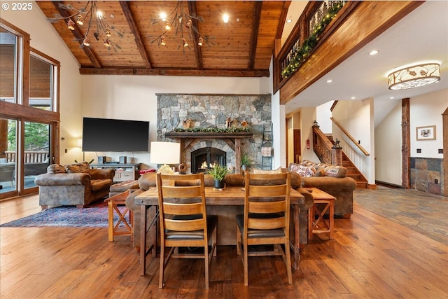 dining space with wooden ceiling, beamed ceiling, high vaulted ceiling, wood-type flooring, and a stone fireplace