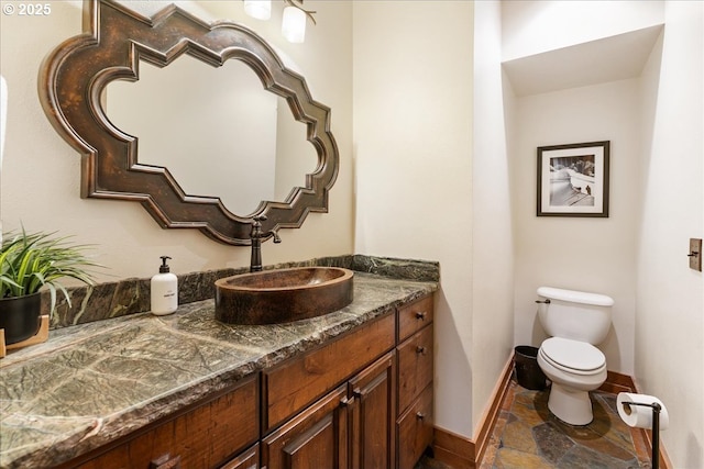 bathroom featuring baseboards, stone tile floors, toilet, and vanity