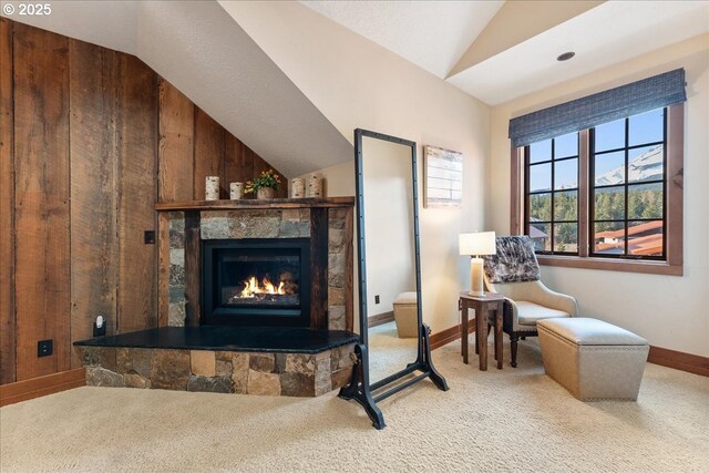 living area with vaulted ceiling, carpet flooring, a fireplace, baseboards, and wooden walls