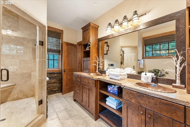 full bath with a shower stall, double vanity, healthy amount of natural light, and stone tile floors