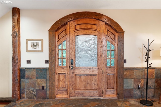 foyer entrance featuring stone tile flooring, wainscoting, and healthy amount of natural light