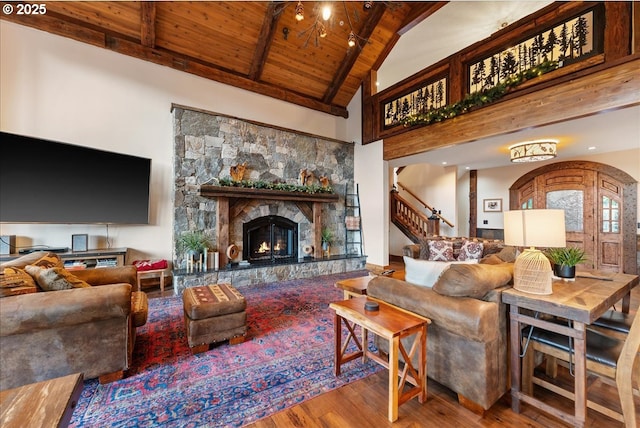 living area featuring wooden ceiling, wood finished floors, beamed ceiling, stairway, and a stone fireplace