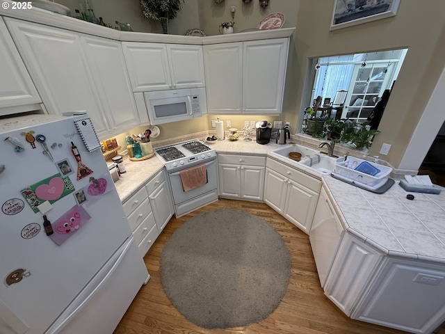 kitchen with tile counters, white cabinets, a sink, wood finished floors, and white appliances