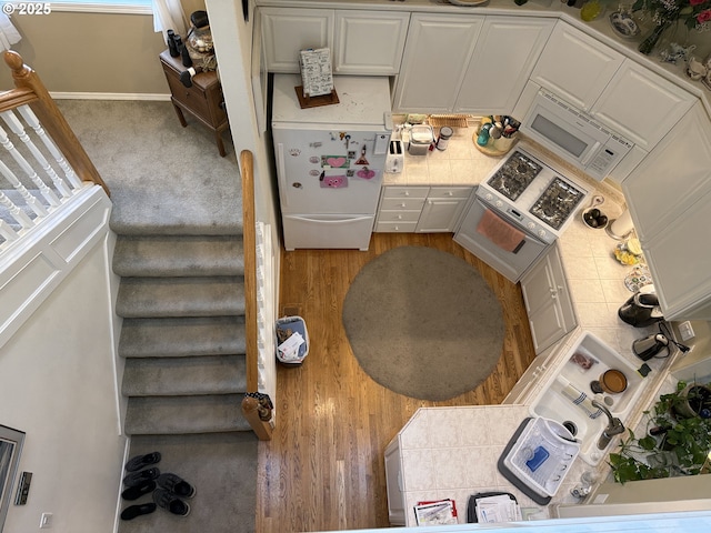 kitchen featuring white appliances, white cabinets, tile countertops, and baseboards