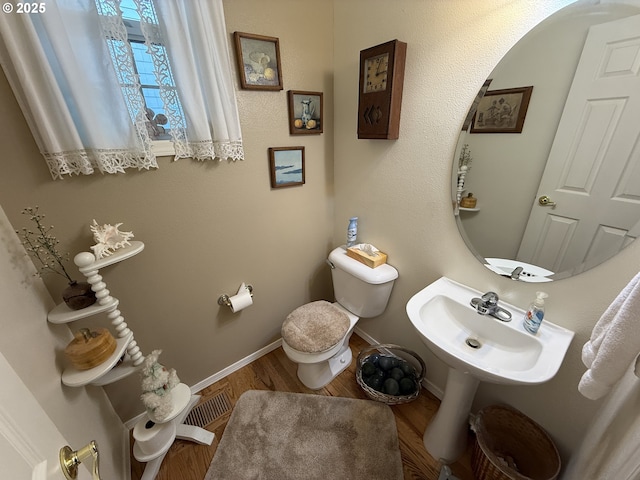 half bathroom with toilet, a sink, baseboards, and wood finished floors