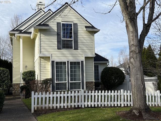 traditional home with stone siding, a fenced front yard, and a chimney