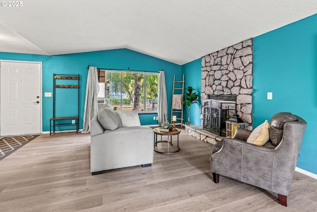 living room with a textured ceiling, vaulted ceiling, baseboards, wood finished floors, and a stone fireplace