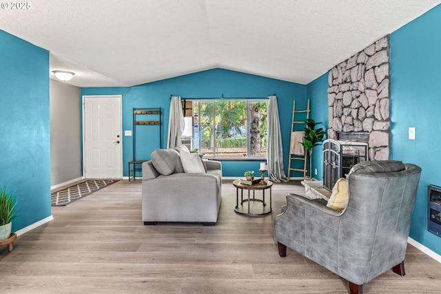 living area with lofted ceiling, a stone fireplace, wood finished floors, baseboards, and a textured ceiling