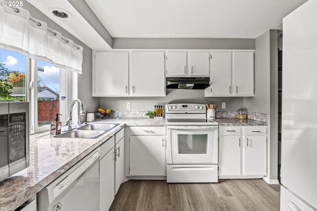 kitchen featuring white cabinets, under cabinet range hood, a sink, white appliances, and light wood-style flooring