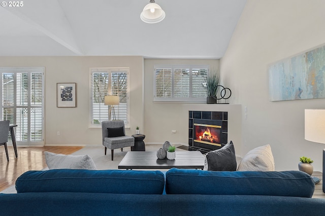 living area featuring a tiled fireplace, lofted ceiling, wood finished floors, and baseboards