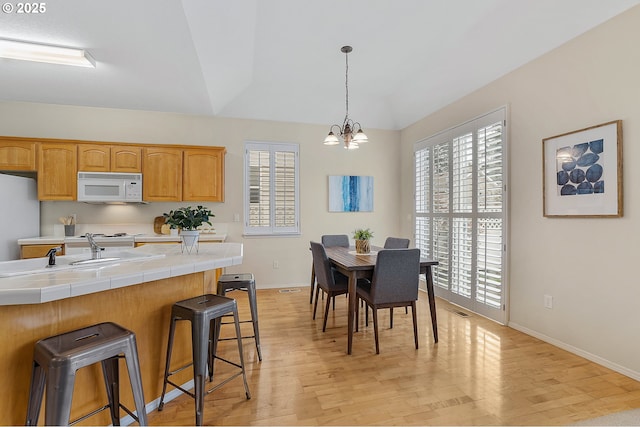 dining space featuring light wood finished floors, a notable chandelier, baseboards, and visible vents