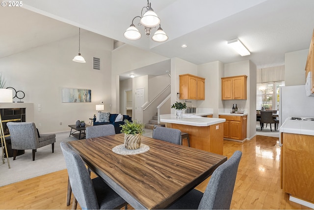 dining area featuring stairway, visible vents, light wood finished floors, an inviting chandelier, and a tile fireplace