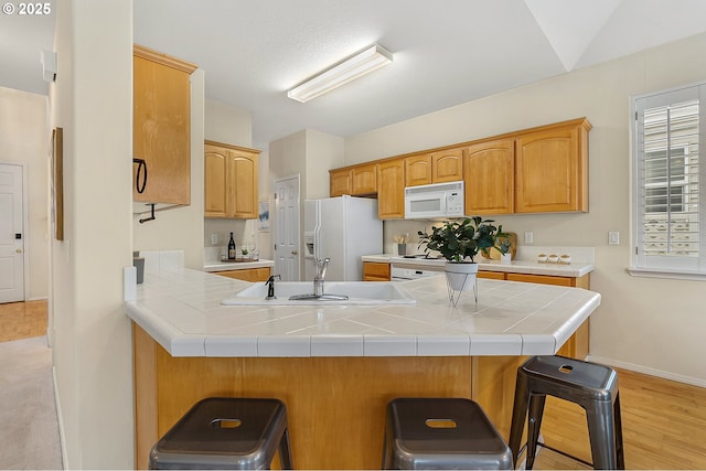 kitchen featuring white appliances, baseboards, a peninsula, a sink, and a kitchen bar