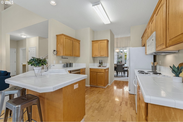 kitchen with a breakfast bar, light wood-style flooring, a sink, a peninsula, and white microwave