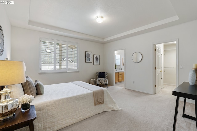 bedroom with a raised ceiling, connected bathroom, baseboards, and light carpet