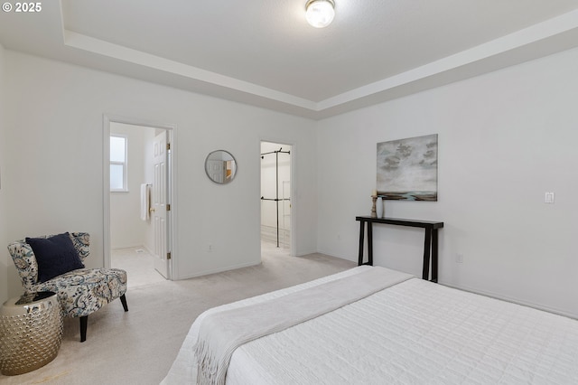 bedroom featuring a tray ceiling, baseboards, light colored carpet, and ensuite bathroom