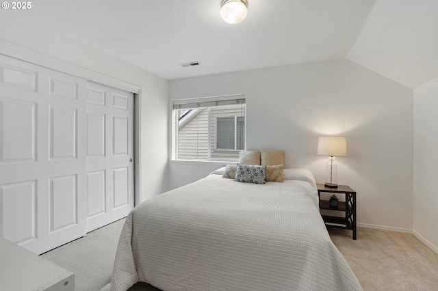 bedroom featuring visible vents, baseboards, light colored carpet, lofted ceiling, and a closet