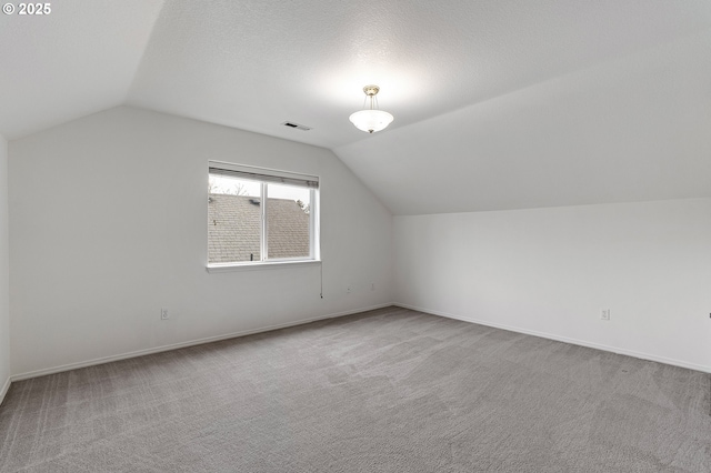 additional living space featuring baseboards, visible vents, carpet floors, vaulted ceiling, and a textured ceiling