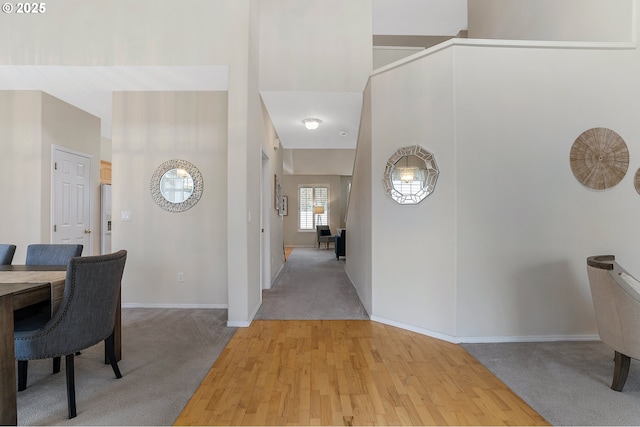 hall with light colored carpet, baseboards, a high ceiling, and light wood-style floors