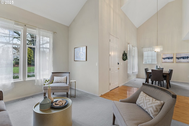 carpeted living area with visible vents, baseboards, a notable chandelier, and high vaulted ceiling