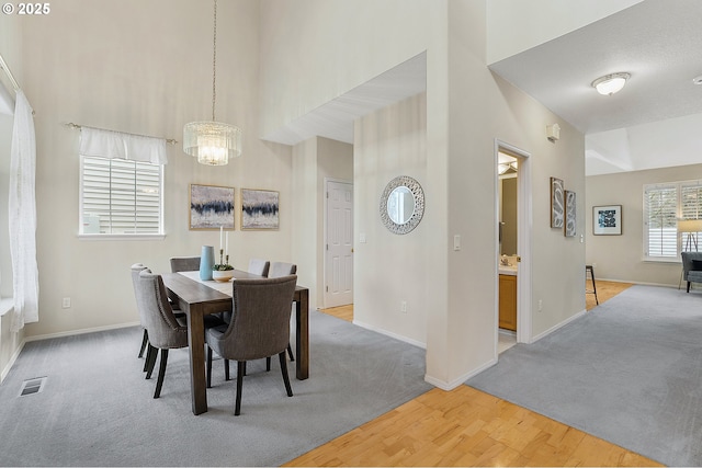 dining room with baseboards, visible vents, an inviting chandelier, a high ceiling, and light carpet