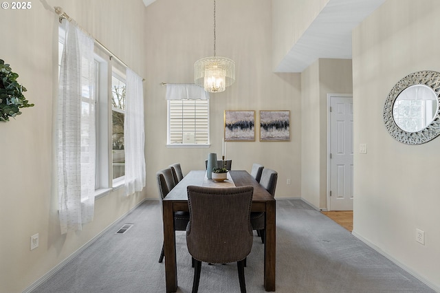 carpeted dining area with a chandelier, visible vents, a high ceiling, and baseboards