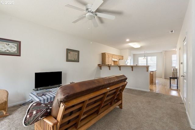 living area with light colored carpet, visible vents, a ceiling fan, and baseboards