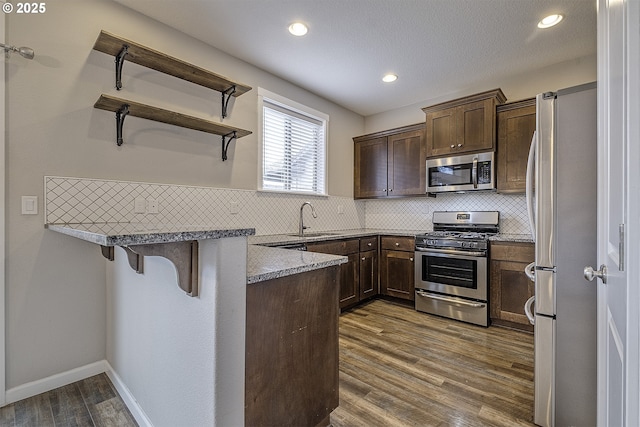 kitchen featuring a breakfast bar, dark wood finished floors, stainless steel appliances, a sink, and a peninsula