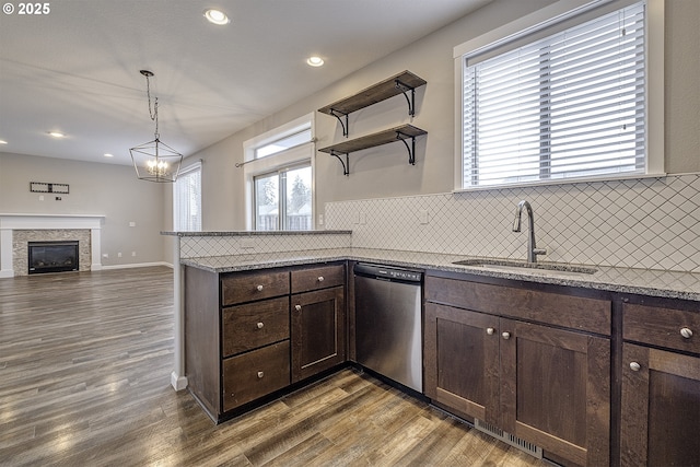 kitchen with decorative light fixtures, dark wood finished floors, stainless steel dishwasher, a sink, and dark stone countertops