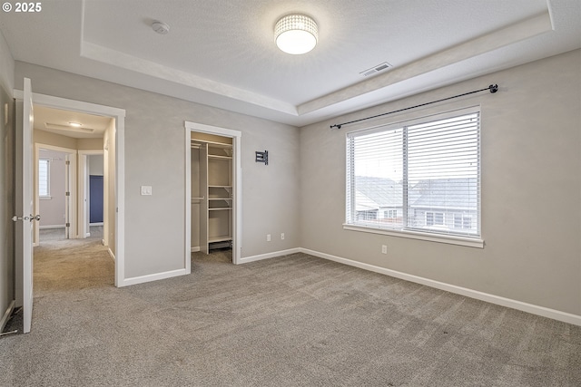 unfurnished bedroom featuring light carpet, visible vents, baseboards, a tray ceiling, and a walk in closet