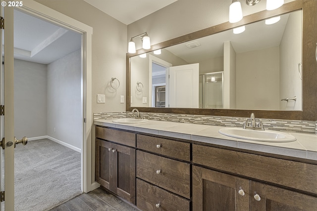 bathroom featuring double vanity, baseboards, a sink, and a shower with shower door