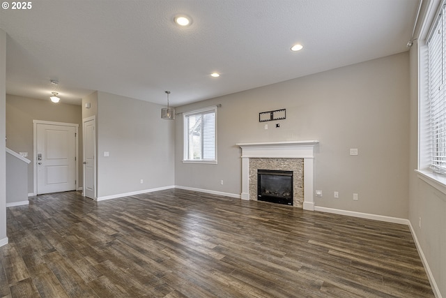 unfurnished living room featuring dark wood-style floors, recessed lighting, a tiled fireplace, a textured ceiling, and baseboards