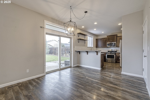 kitchen with a breakfast bar area, a peninsula, visible vents, appliances with stainless steel finishes, and decorative light fixtures