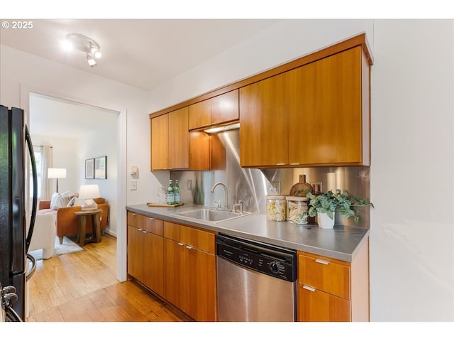 kitchen featuring a sink, stainless steel countertops, light wood-style flooring, freestanding refrigerator, and stainless steel dishwasher
