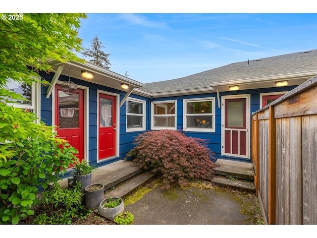 doorway to property featuring fence and roof with shingles
