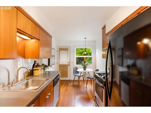 kitchen featuring brown cabinets, stainless steel appliances, a sink, and light wood-style floors