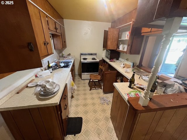 kitchen featuring a peninsula, black microwave, white range with electric cooktop, light floors, and light countertops