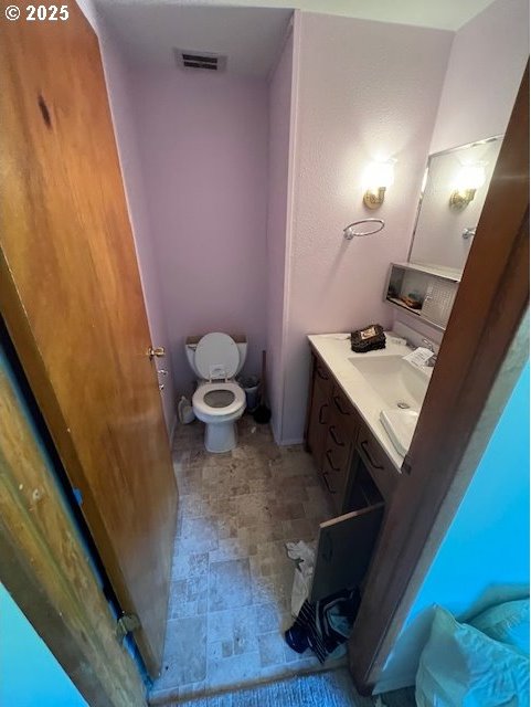 bathroom with visible vents, stone finish flooring, toilet, and vanity
