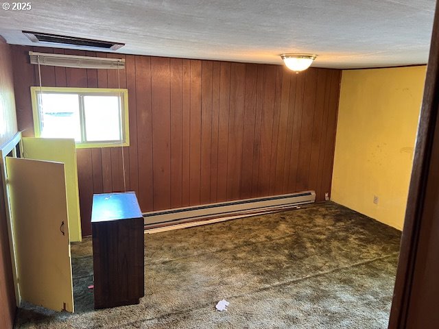 empty room with a baseboard radiator, carpet, wood walls, and visible vents