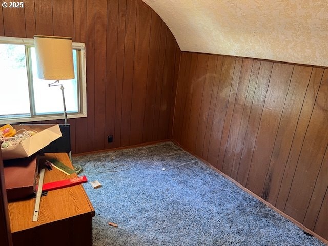 bonus room featuring carpet, vaulted ceiling, and wood walls
