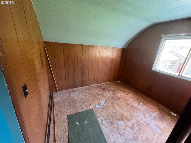 additional living space featuring a textured ceiling, wood walls, and lofted ceiling