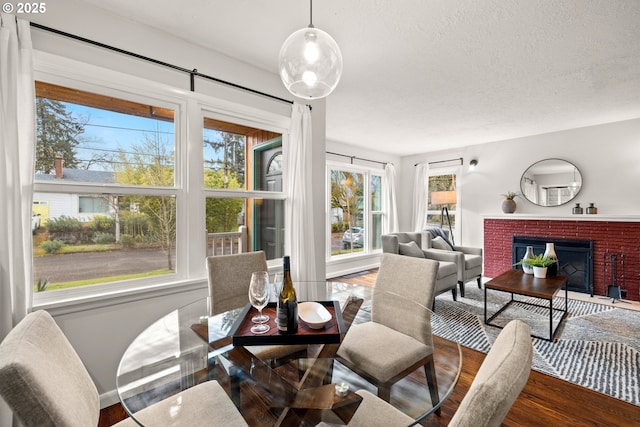 dining space featuring a brick fireplace, wood finished floors, and a textured ceiling